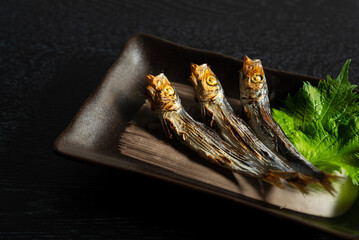Grilled urume sardines on a black table. A side dish of sake.