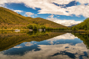 Fototapeta na wymiar The crystal clear reflections on the beautiful serene little Boat Harbour at Sailors Cutting , Lake Benmore NZ