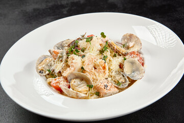 Seafood pasta with vongole, clams, salmon fish and prawns in white plate. Spaghetti marinara with seafood and cheese on dark background. Seafood menu -  pasta in mediterrian  style on black table.