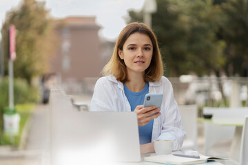 Beautiful smiling woman holding mobile phone, chatting, communication online sitting in street cafe 