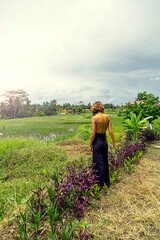 Fototapeta premium Caucasian woman, blonde, in yellow and black dress standing among the flowers and rice fields.
