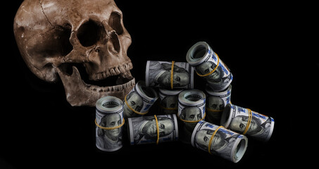 Human skull and rolled stacks of 100 American dollars bills on a black background