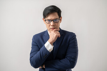 Portrait of serious Asian businessman in glasses thinking with hand on chin isolated on white background