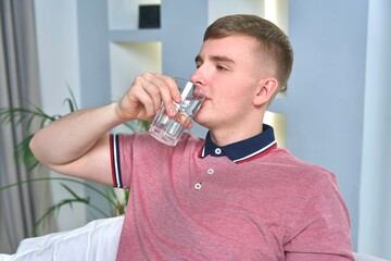 Fototapeta na wymiar Young man is drinking pure fresh water from glass at home in living room