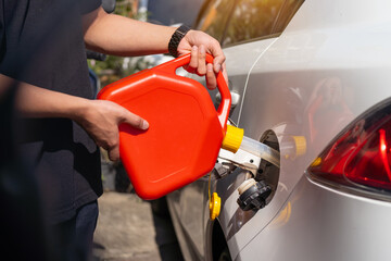 Man fills the fuel into the gas tank of car from a red canister or plastic fuel cann .maintenance...