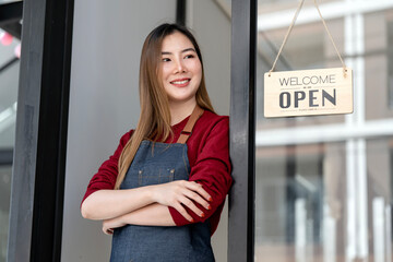 Portrait of positive business woman standing at cafeteria door entrance. Cheerful young waitress in blue apron near glass door with open signboard.