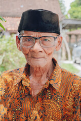 A portrait of an old Asian man wearing batik shirt and glasses