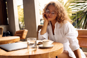 Online Education At Cafe. Happy Girl In Casual Clothes And Glasses Preparing Writing. Remote Job Or Education With Modern Digital Technologies For Comfortable Lifestyle In City