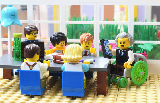 Lego minifigures at business meeting on table, the chef in in a invalid chair. Editorial illustrative image of people are planning in office.