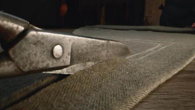 Close-up shot of tailor cutting fabric according to sketch using scissors for sewing. Process of making clothes in luxury designer atelier or tailoring studio. Fashion and hand craft concept.