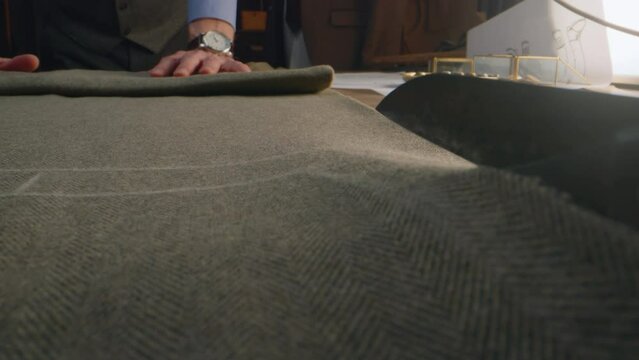 Close-up shot of tailor cutting textile according to sketch using scissors for sewing. Process of making clothes in luxury designer atelier or tailoring studio. Fashion and hand craft concept.