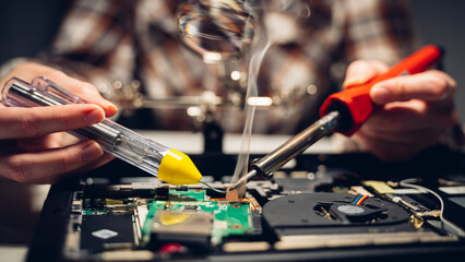 a computer master solders a chip and a board on a laptop, the concept of electronics repair shops