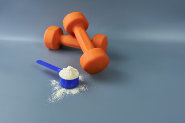 Orange dumbbells with a portion of vanilla whey protein on a gray background. The concept is protein nutrition. 