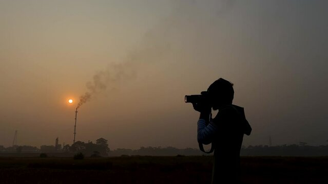 Medium close up of man photographing industrial area, hazy sunset, static