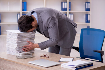 Young male employee and too much work at workplace
