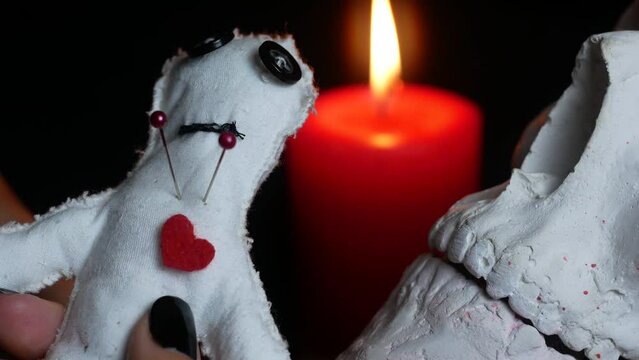 Seance with voodoo doll and curse. Red candles, black background, scary atmosphere in the frame.