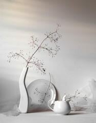 Modern still life scene with dry branch and ceramic vase on white background. Background in sunlight