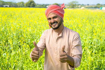 Happy smiling farmer showing thumbs up gesture by looking at camera at farmlad - concept of small...