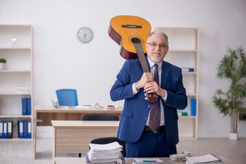 Old male employee playing guitar at workplace