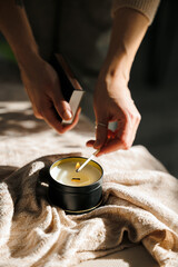 Soy scented candles in metal jars, boxes. The candle is lit by a girl. A long match burns.  Modern...