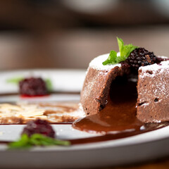 Chocolate fondant on plate. Dessert in cut form, decorated with mint and powdered sugar. French dessert. Close-up. Side view. Soft focus. 