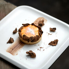 Small round dessert on plate. White square plate with dish on table. Pastry is decorated with chocolate and powdered sugar. Serving dessert in restaurant. Close-up. Top view. 