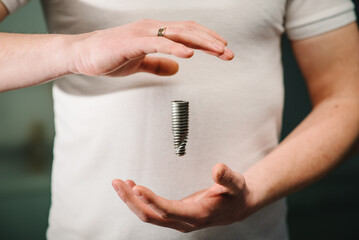 Dental implant. Dentist hold a model of dental implant in hand.  Concept of implantation teeth and dental surgery. Space for text. Hand showing the installation of a dental implant. Closeup.