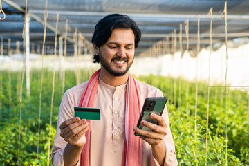 Happy Indian farmer with Green card using mobile phone at greenhouse - concept of online banking, application and technology