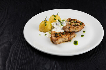 Grilled pork meat with mushroom sauce and potato on white plate on wooden black background