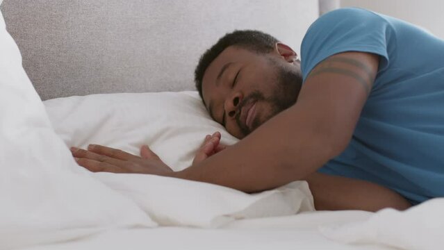 Close up portrait of young african american man lying on bed and making himself comfortable, sleeping alone, empty space