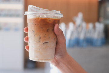 Close up of Hand holding a glass of Iced latte or cappuccinos in the middle with coffee shop background. Concept of promoted coffee shop or cafe with copy space and wide screen, banner.
