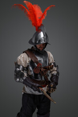 Studio shot of isolated on grey musketeer with sword and pistol dressed in armor.