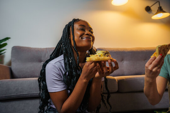 Young woman with slice of delicious pizza sitting on a living room floor