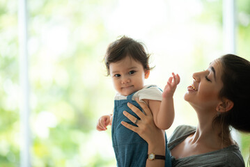 Cute little baby toddler playing and enjoying while in the arms of young mother hugging at home