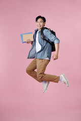 Full length portrait of a funny cheerful male student jumping on pink background