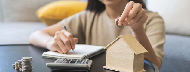 Saving money wealth concept, asian young business woman hand putting coin into box house for saving cost, cash finance planning to spend enough money on her income for save money, payment tax, invest.
