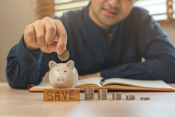 Close up hand of asian young businessman, male putting coin into a piggy ceramic for saving cost,...