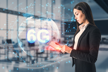 Young businesswoman using tablet with globe and 6g hologram on blurry office interior background. Telecommunication and internet speed concept. Double exposure.