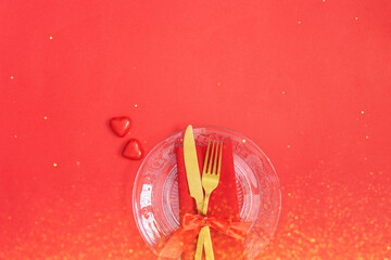 Festive table setting with Gold cutlery and crystal plate, red hearts and gift on red background.Saint Valentines day celebration or romantic dinner concept.