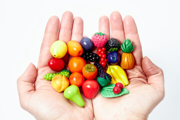 Hands hold children's toys in the form of handmade vegetables. On a white background.