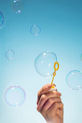 Close up side view shot of young man blowing soap bubbles on blue background. Focus on hand and...