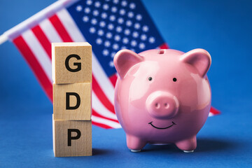 Piggy bank, wooden cubes with text and a flag on a blue background, a concept on the theme of the GDP of the United States of America