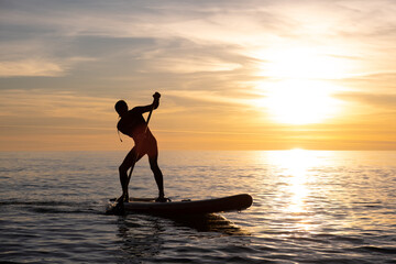 a sporty guy swims with a paddle on a sapboard in the sea under the beautiful sunset sun