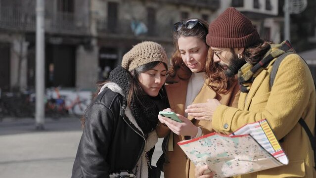 Young friends looking at cell phone and checking city map direction during winter vacations 