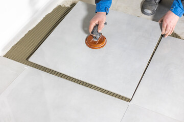 Tiler worker placing or tiling gray ceramic tile in the position over adhesive glue with lash tile...