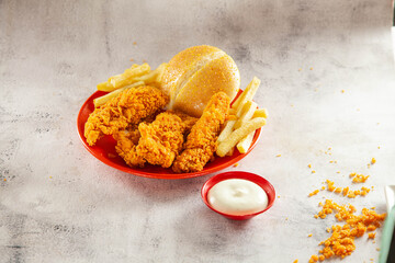 Breaded chicken fillet golden strips in a steel grill basket with mayonnaise dip served on red...