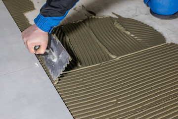 Tiler worker placing or tiling gray ceramic tile in the position over adhesive glue with lash tile leveling system, renovation or recontruction, concept of building