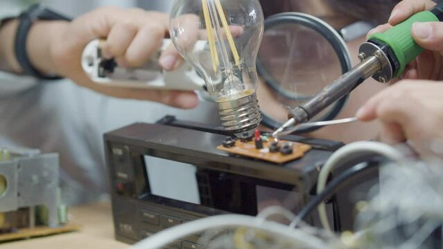 Closeup shot of two schoolchildren doing engineering project together. Dark-haired boy in glasses using magnifier while looking at soldering contacts on circuit board by classmate. Education concept 