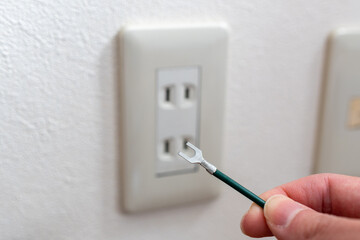 A Japanese wall socket without earth post. Y-shaped ground wire holding by hand. 