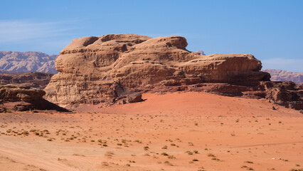 Fototapeta na wymiar Large red sand dunes and rugged sandstone mountainous landscape in remote wilderness of Arabian Wadi Rum desert in Jordan, Middle East